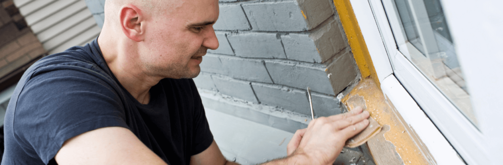 A man is fixing a window on a brick wall.