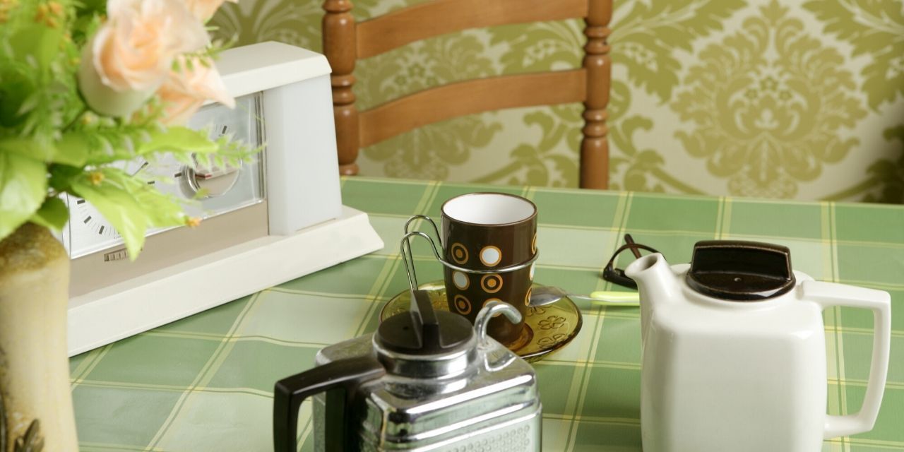 A table with a vase of flowers, a teapot, a cup, and a clock on it.