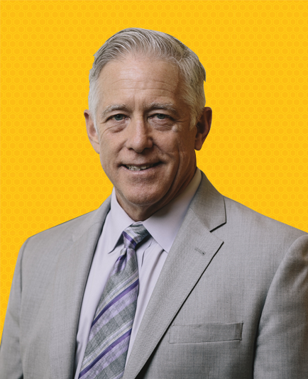 Kurt Reisig, chairman of Mortgage Company, Big Valley Mortgage in a suit and tie is smiling in front of a yellow background.