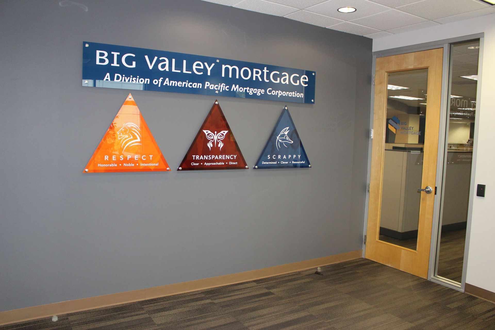 A gray office wall with the Big Valley Mortgage logo and three triangular signs 