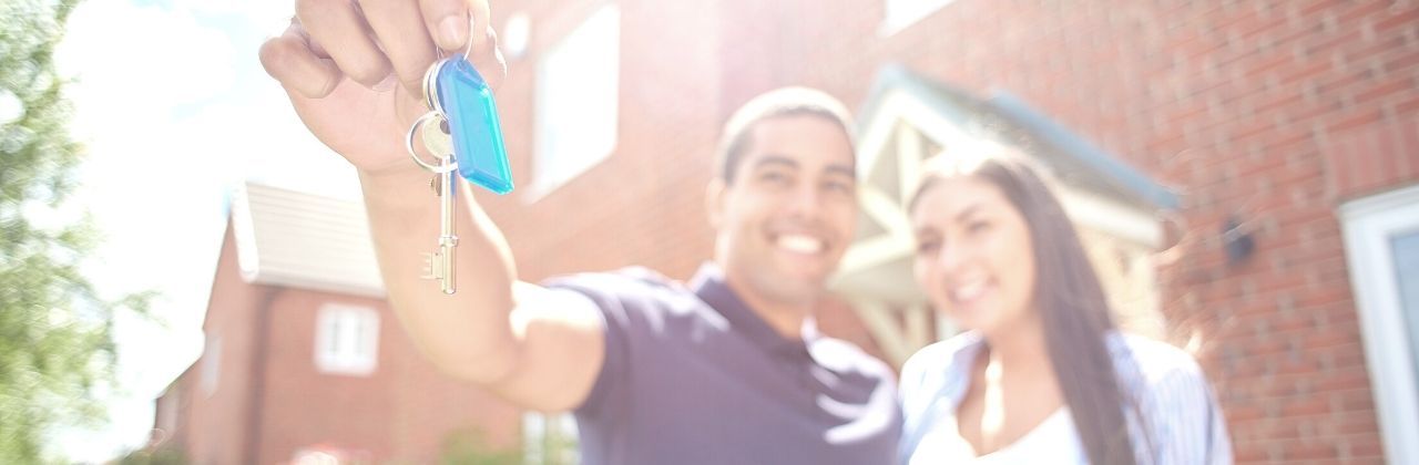 A man and a woman are standing in front of a house holding keys.
