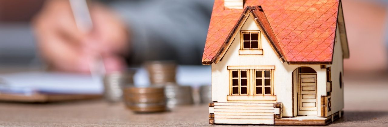 A small wooden house is sitting on a table next to a pile of coins | Home loans in Roseville, CA