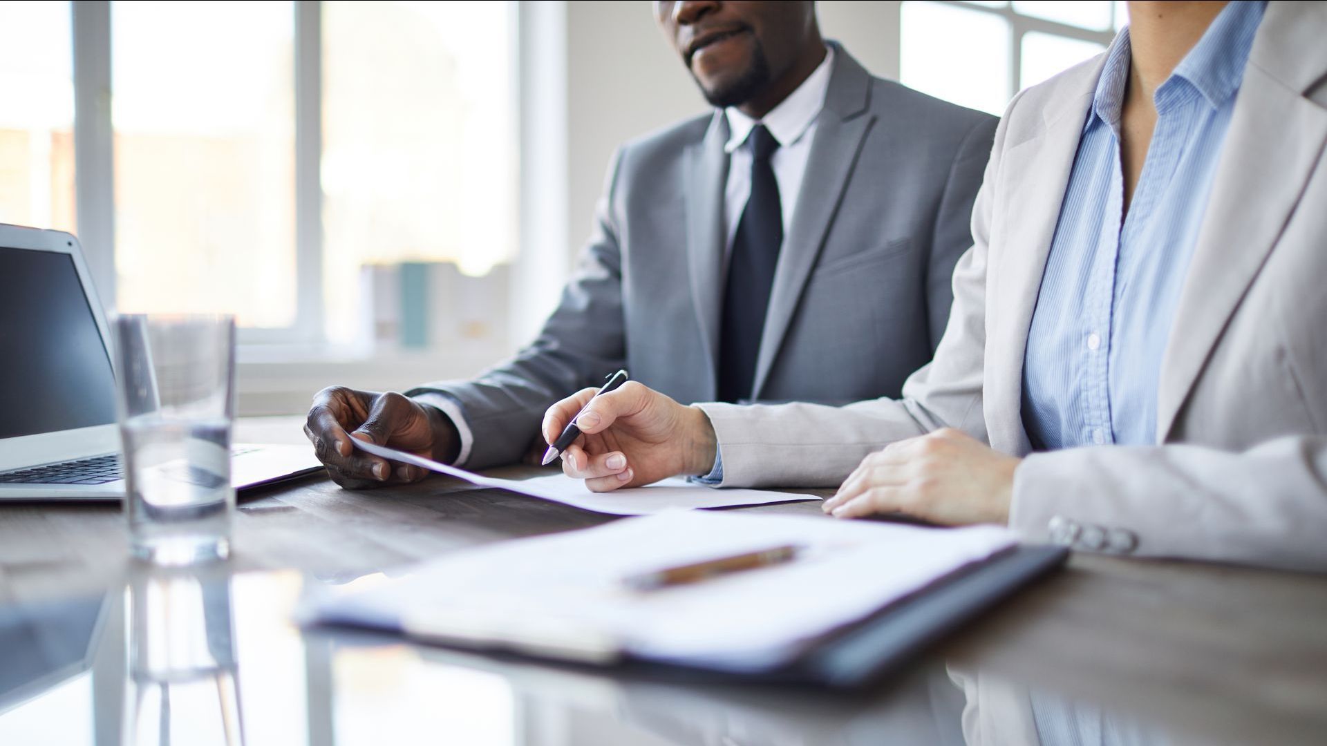 Two businesspeople in suits reviewing documents at a table.