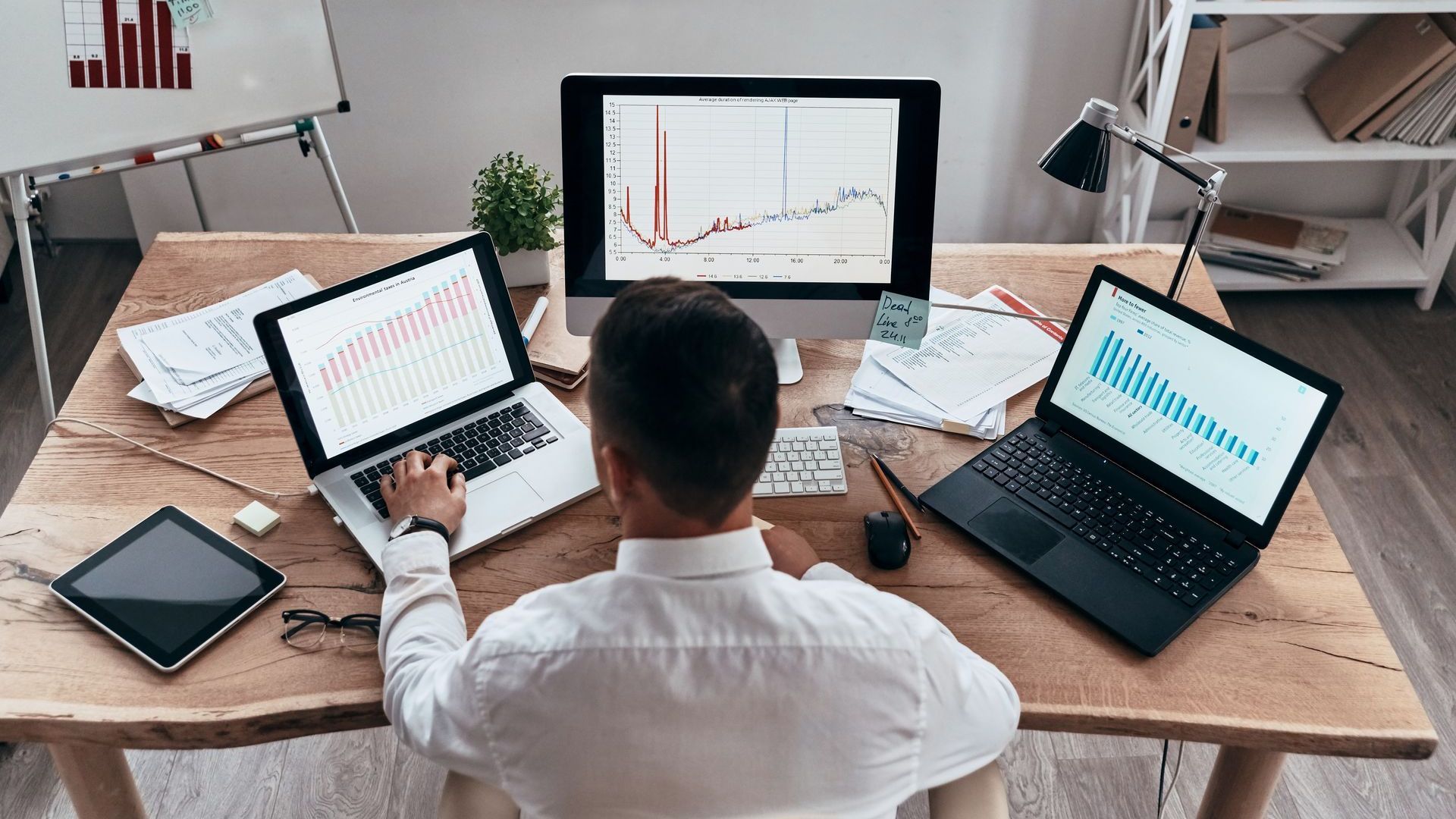 A man is sitting at a desk with two laptops and a computer.