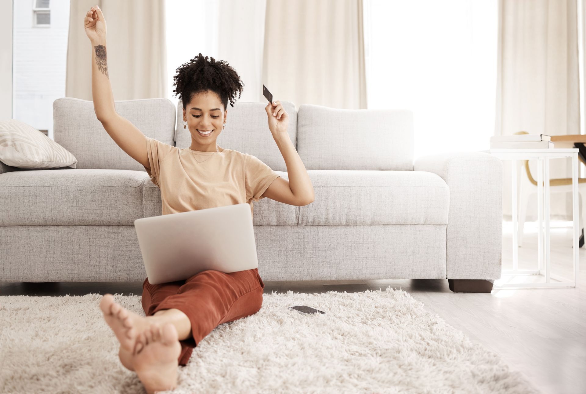A woman is sitting on the floor using a laptop and holding a credit card.