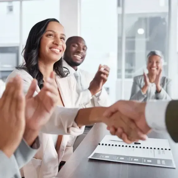  People clapping as two people shake hands in an office, celebrating a deal or agreement.