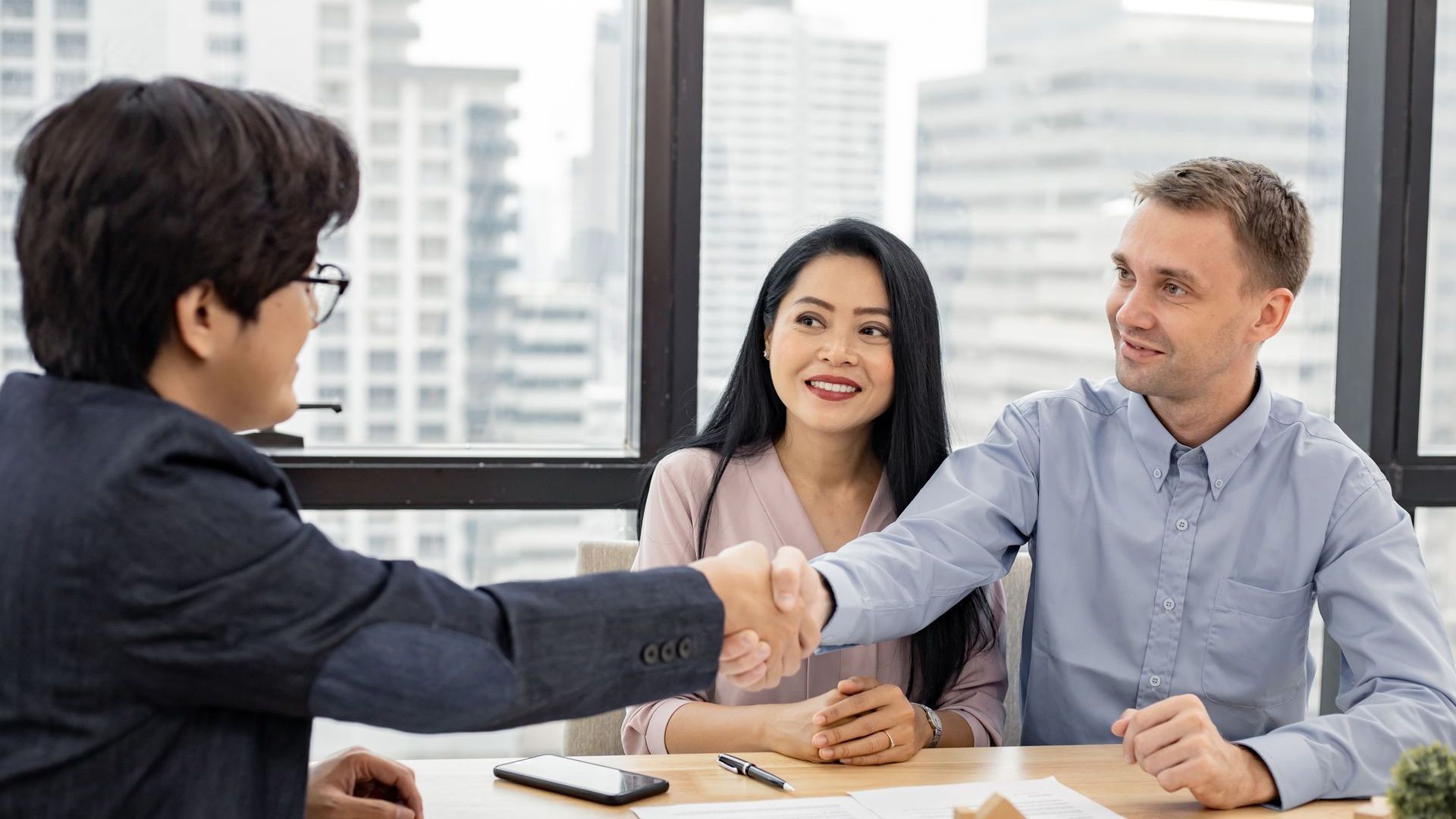 A man is shaking hands with a woman and a man while sitting at a table.