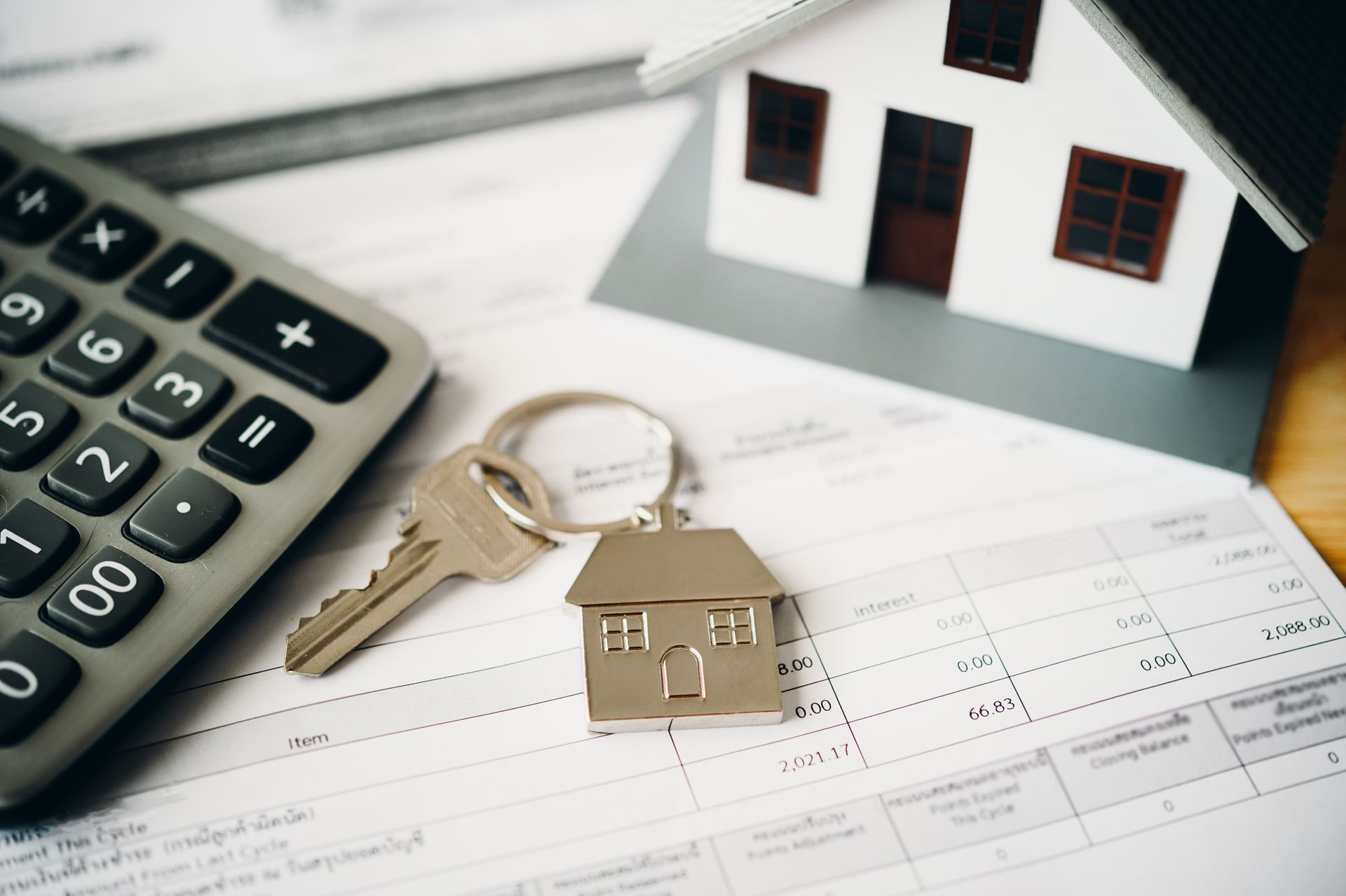 Calculator, house keys, and a miniature house model rest on paperwork.