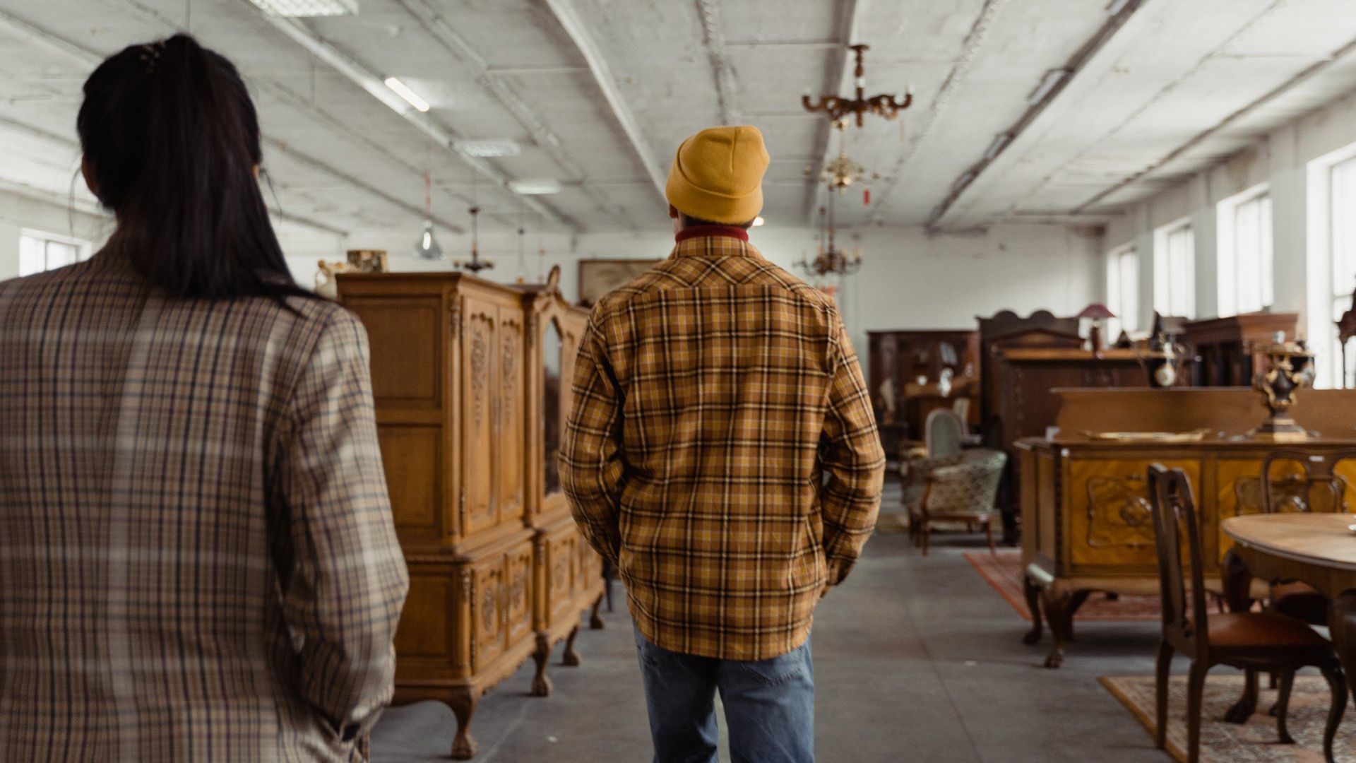 People browse antique furniture in a large, cluttered shop.