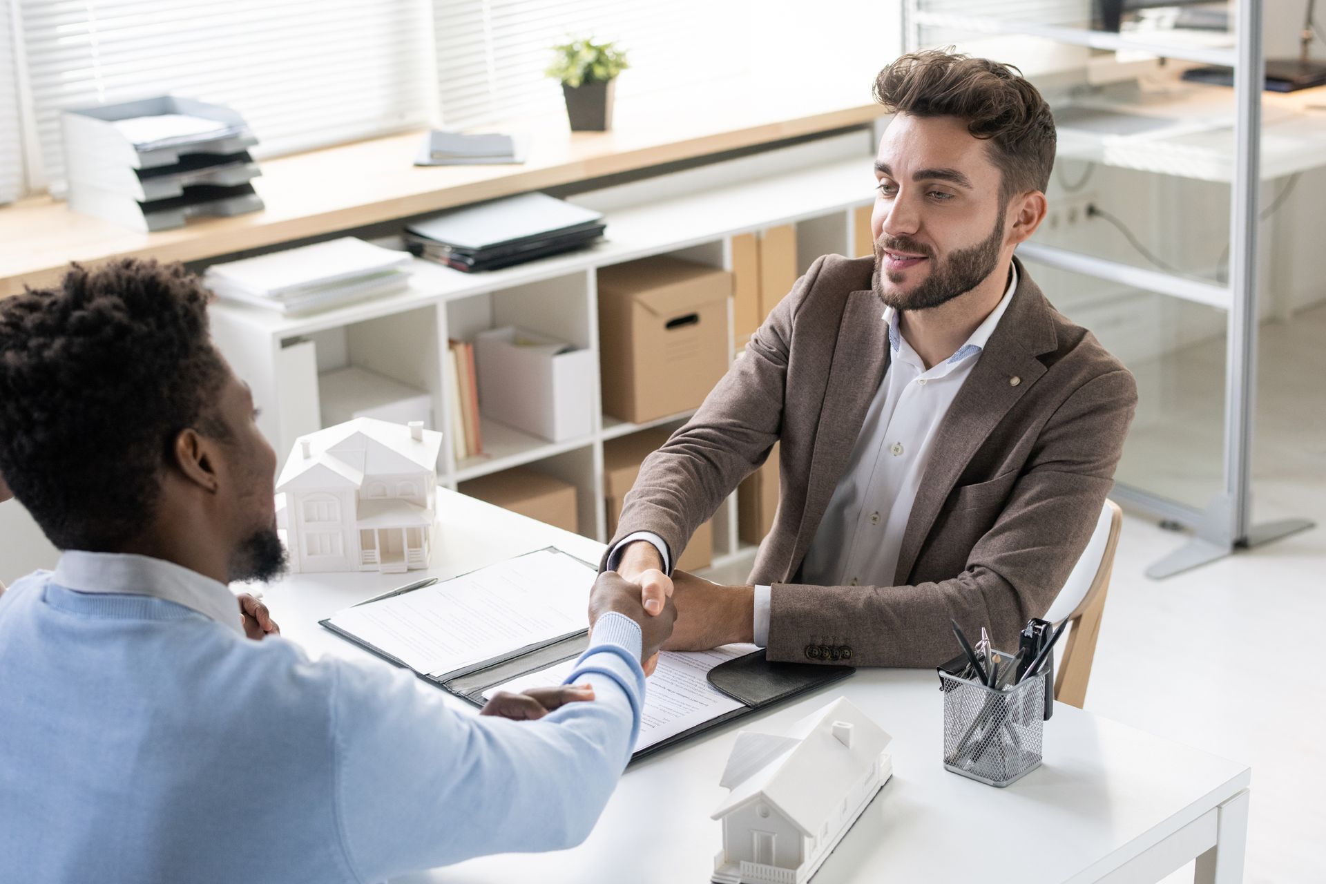 Two men shaking hands at a desk, possibly closing a deal. White office setting.