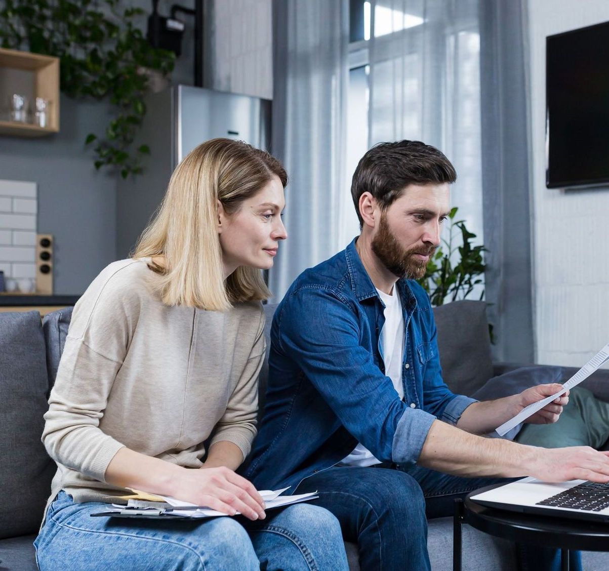 A man and a woman are sitting on a couch looking at a laptop.