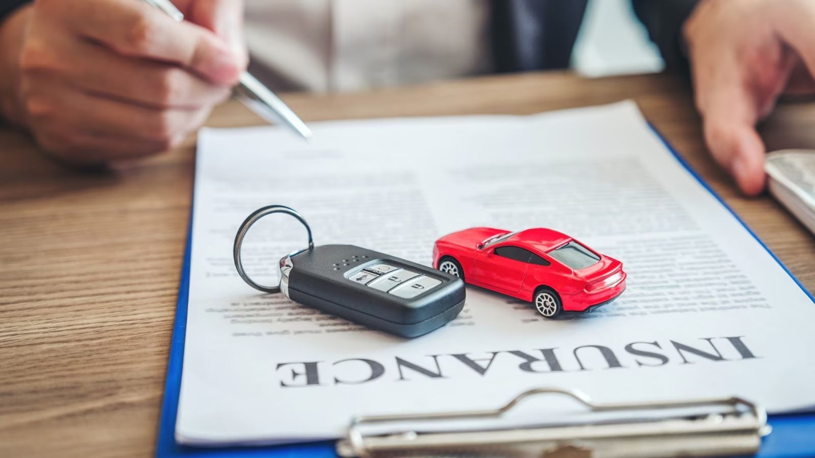 A person is writing on a clipboard with a car key and a toy car on it.
