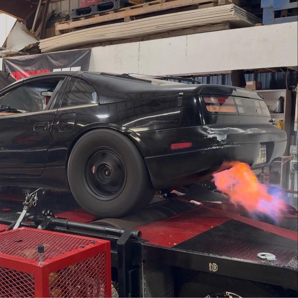 Black sports car on a dyno, shooting flames from the exhaust. Garage setting.