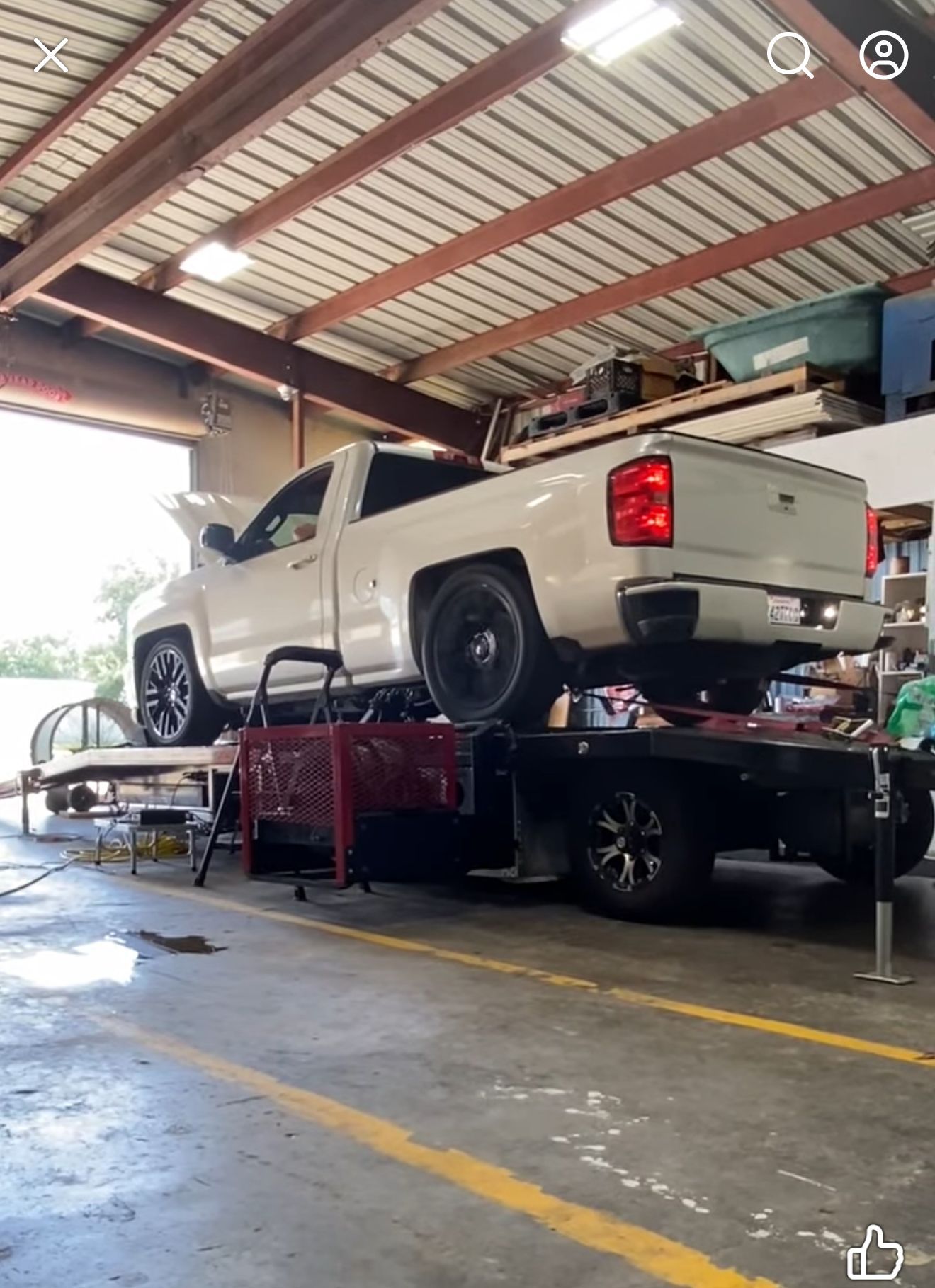 White truck on a lift inside a garage, with the hood open.