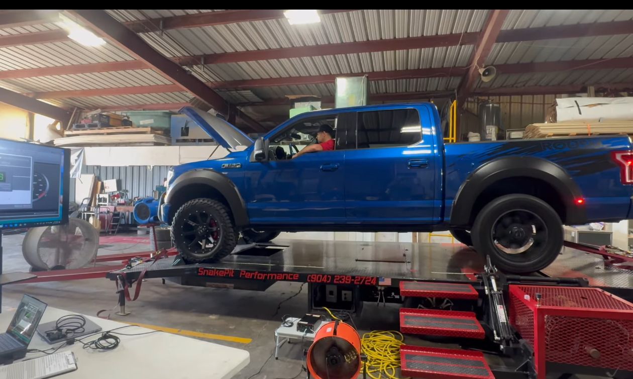 Blue Ford truck on a dynamometer in a shop; a person is inside operating it.