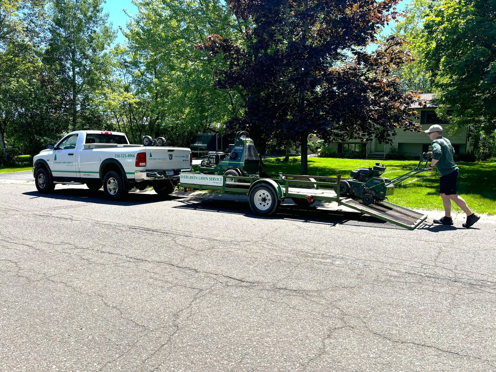 A white truck is towing a trailer with a lawn mower on it.