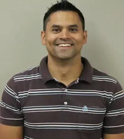 Man smiling, wearing brown and white striped polo shirt, against a gray background.