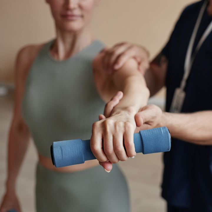Woman lifting weight with assistance from a person, indoors.
