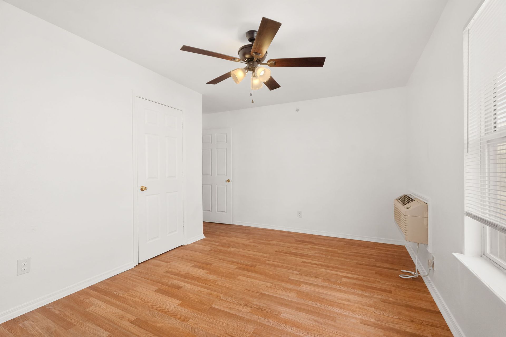 An empty bedroom with hardwood floors and a ceiling fan.