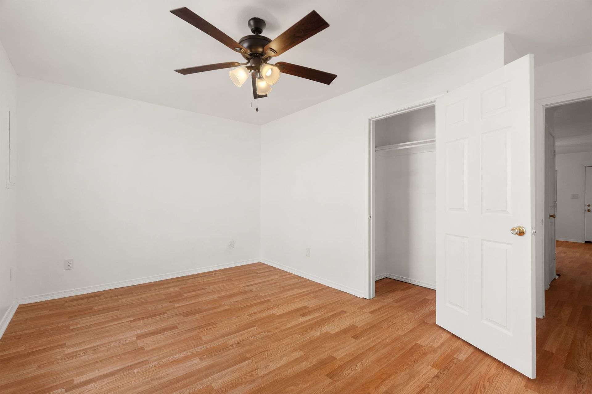 An empty bedroom with hardwood floors and a ceiling fan.