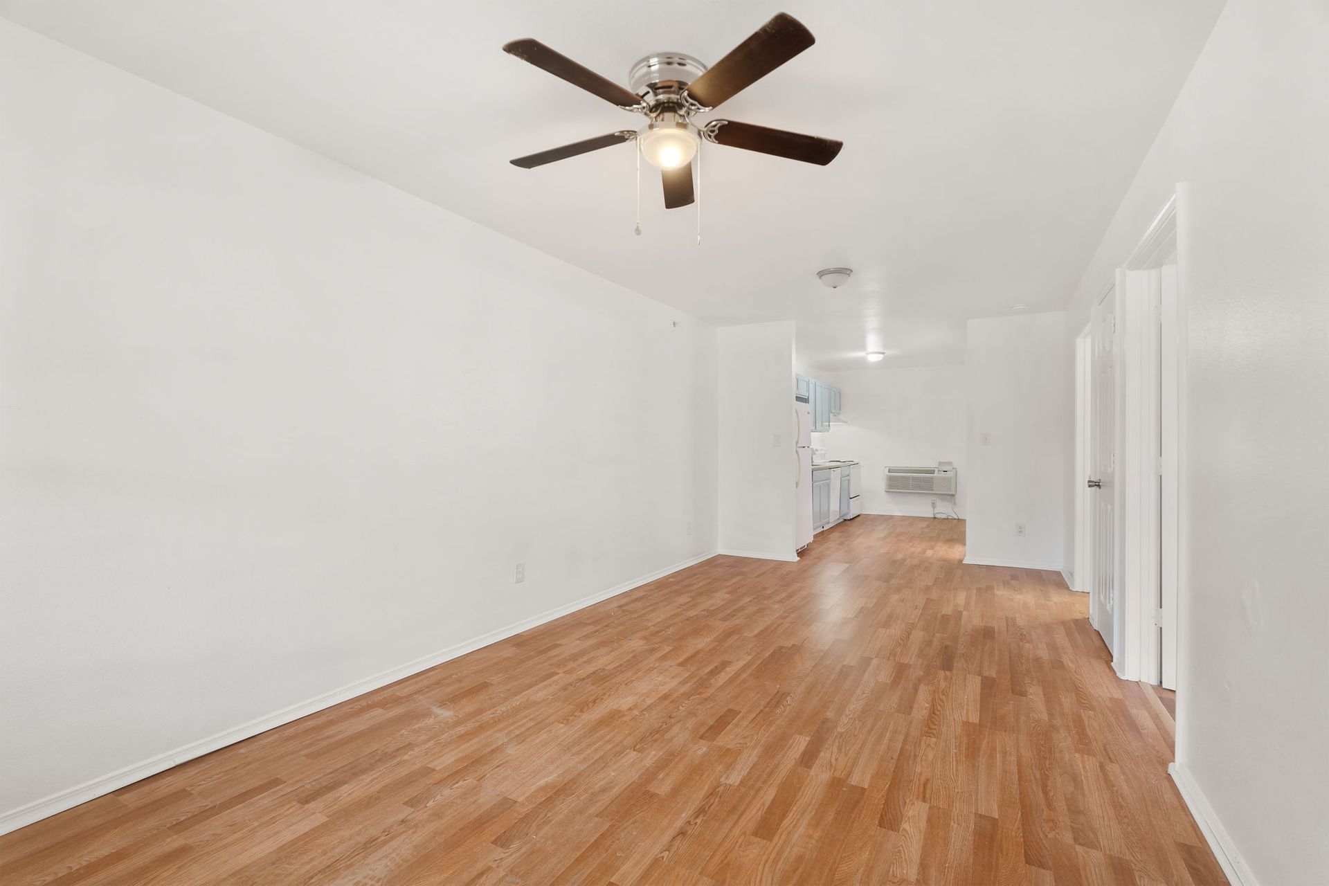 An empty living room with hardwood floors and a ceiling fan