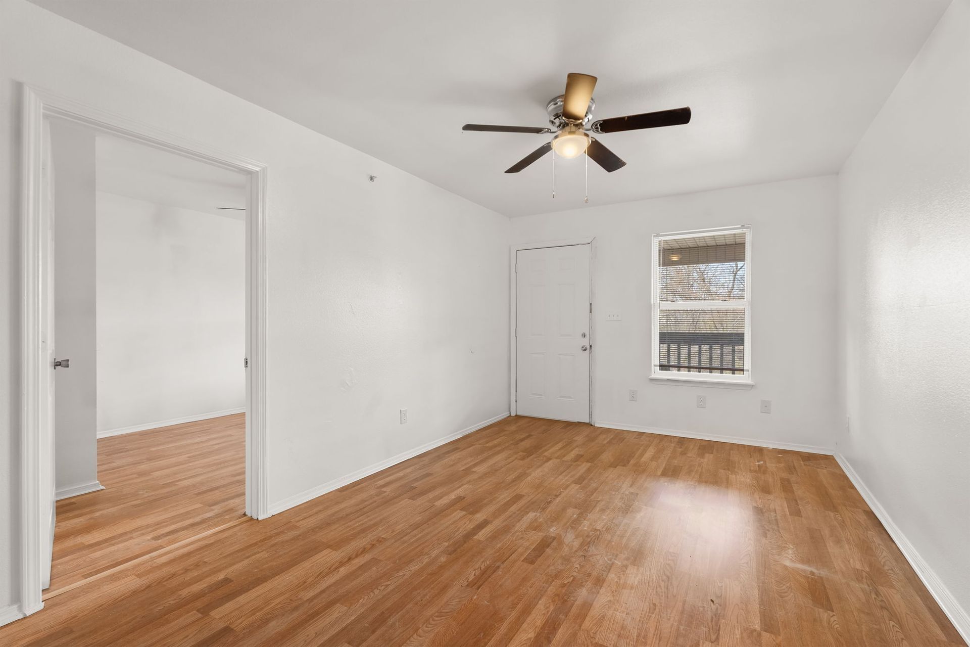 An empty living room with hardwood floors and a ceiling fan.