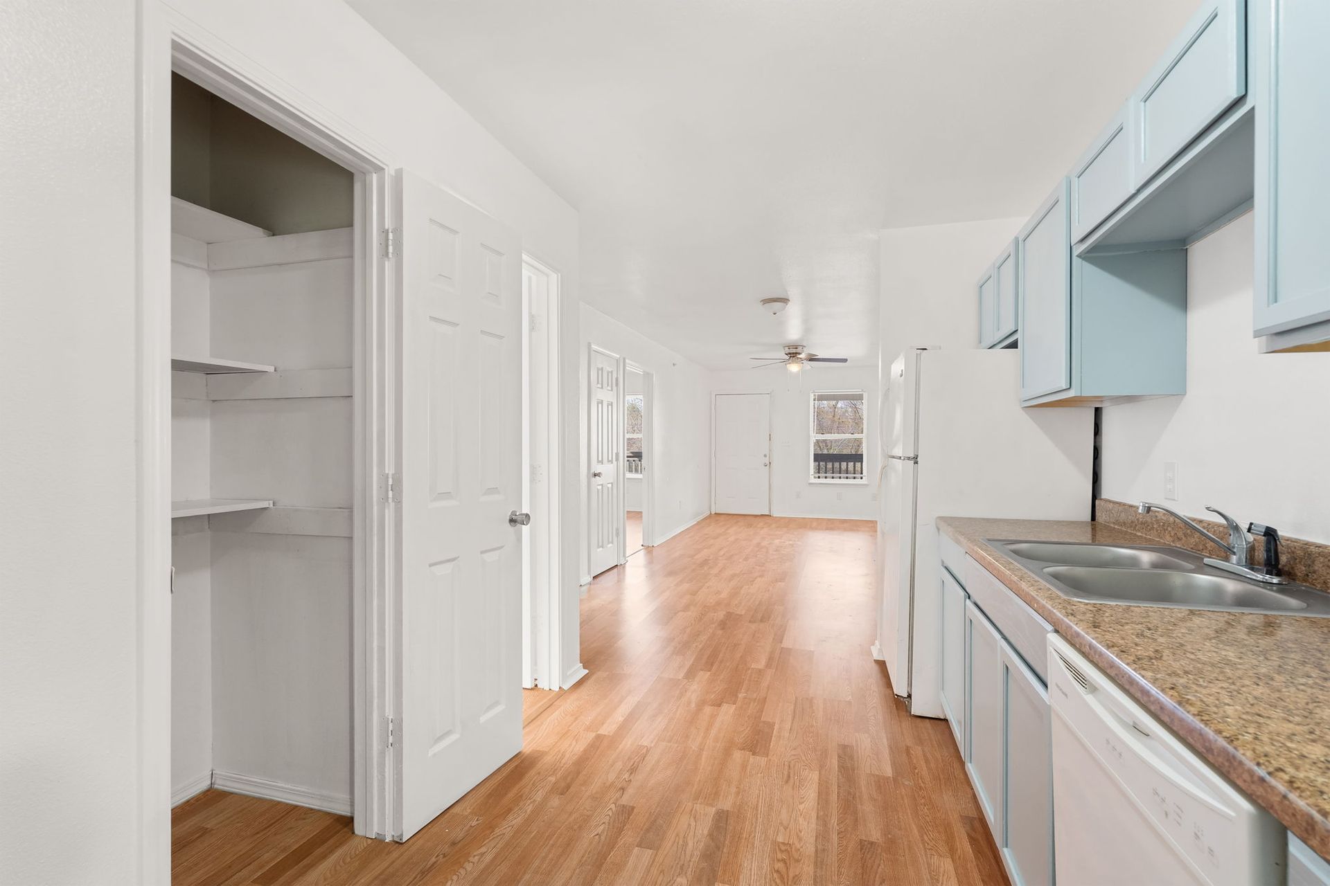 A kitchen with wooden floors , white cabinets , a sink and a dishwasher.