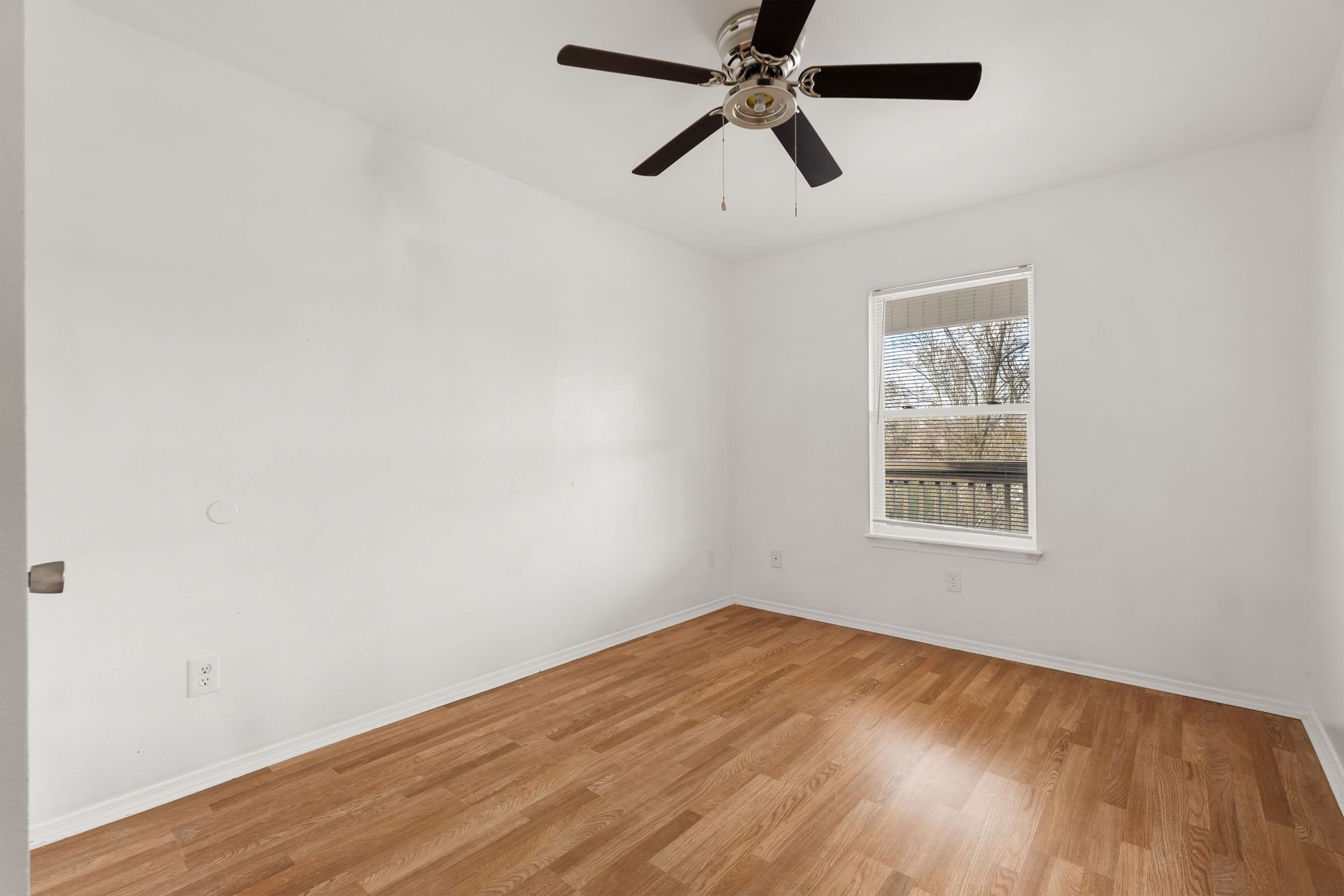 An empty bedroom with hardwood floors and a ceiling fan.
