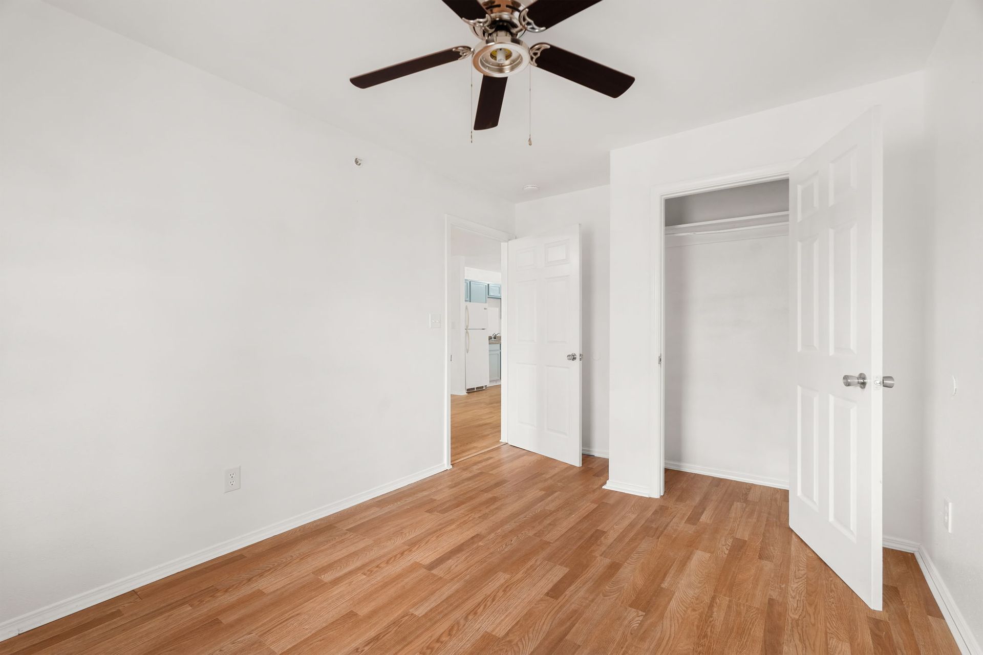 An empty bedroom with hardwood floors and a ceiling fan.