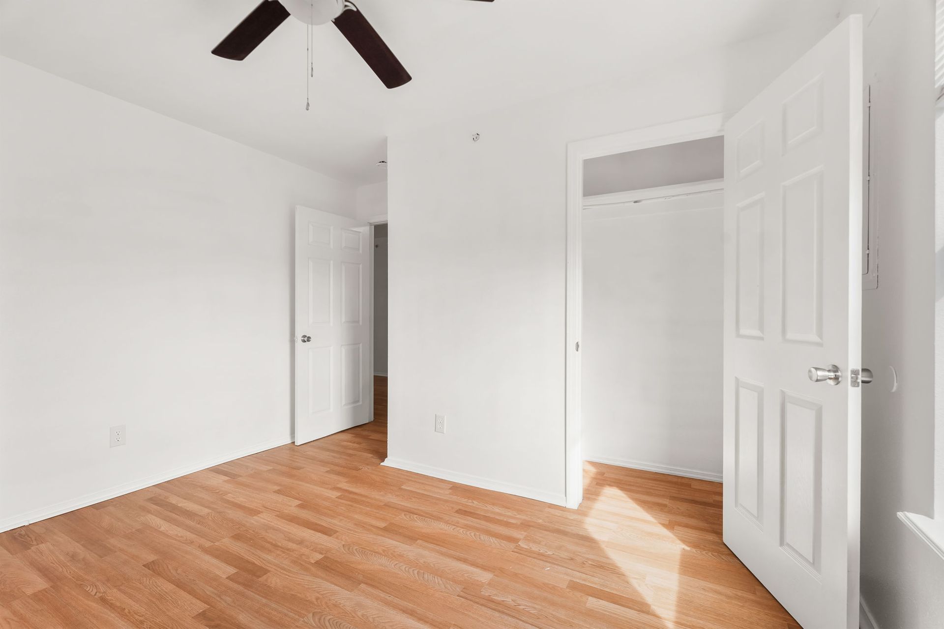 An empty bedroom with hardwood floors and a ceiling fan.