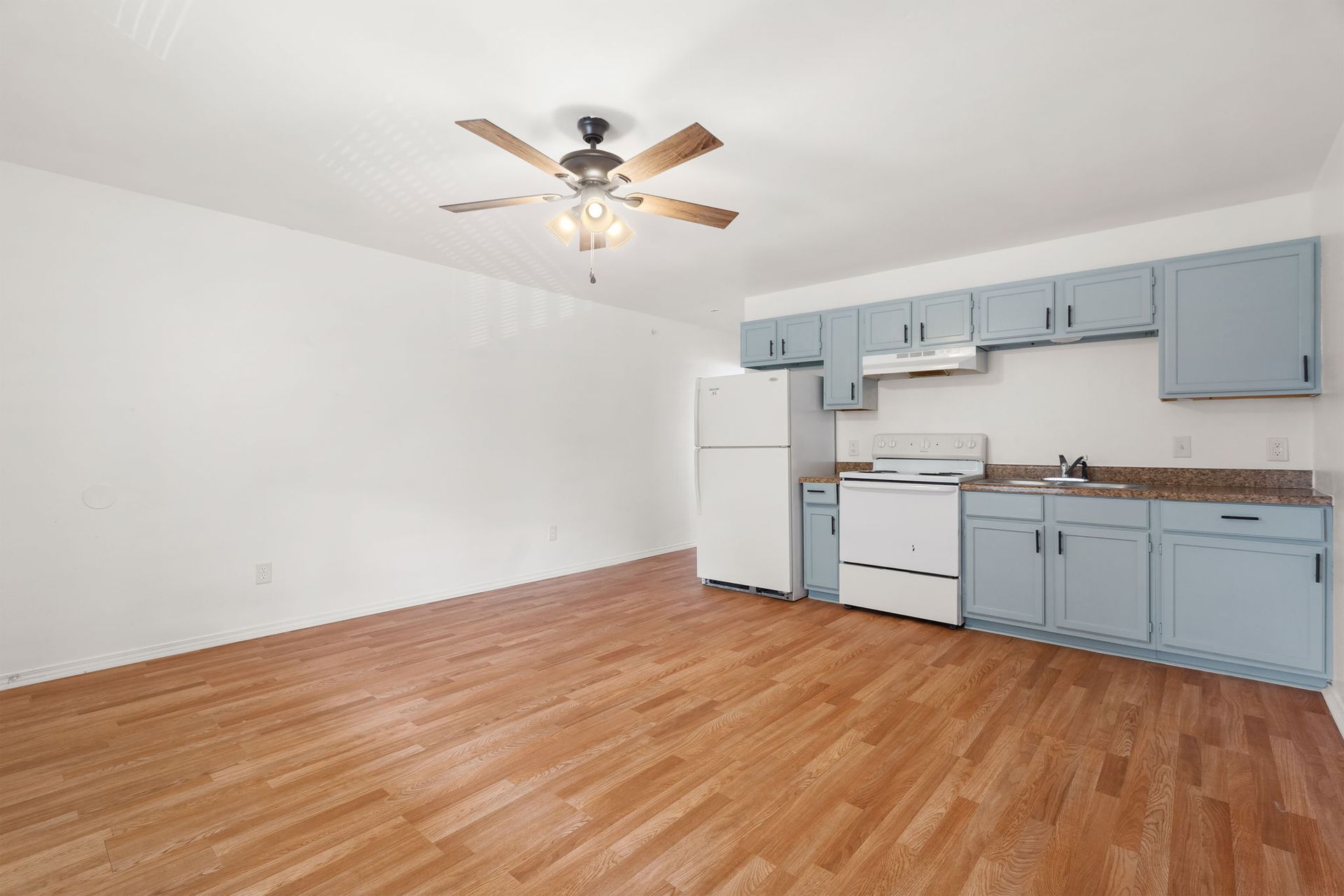 An empty kitchen with blue cabinets and a ceiling fan.