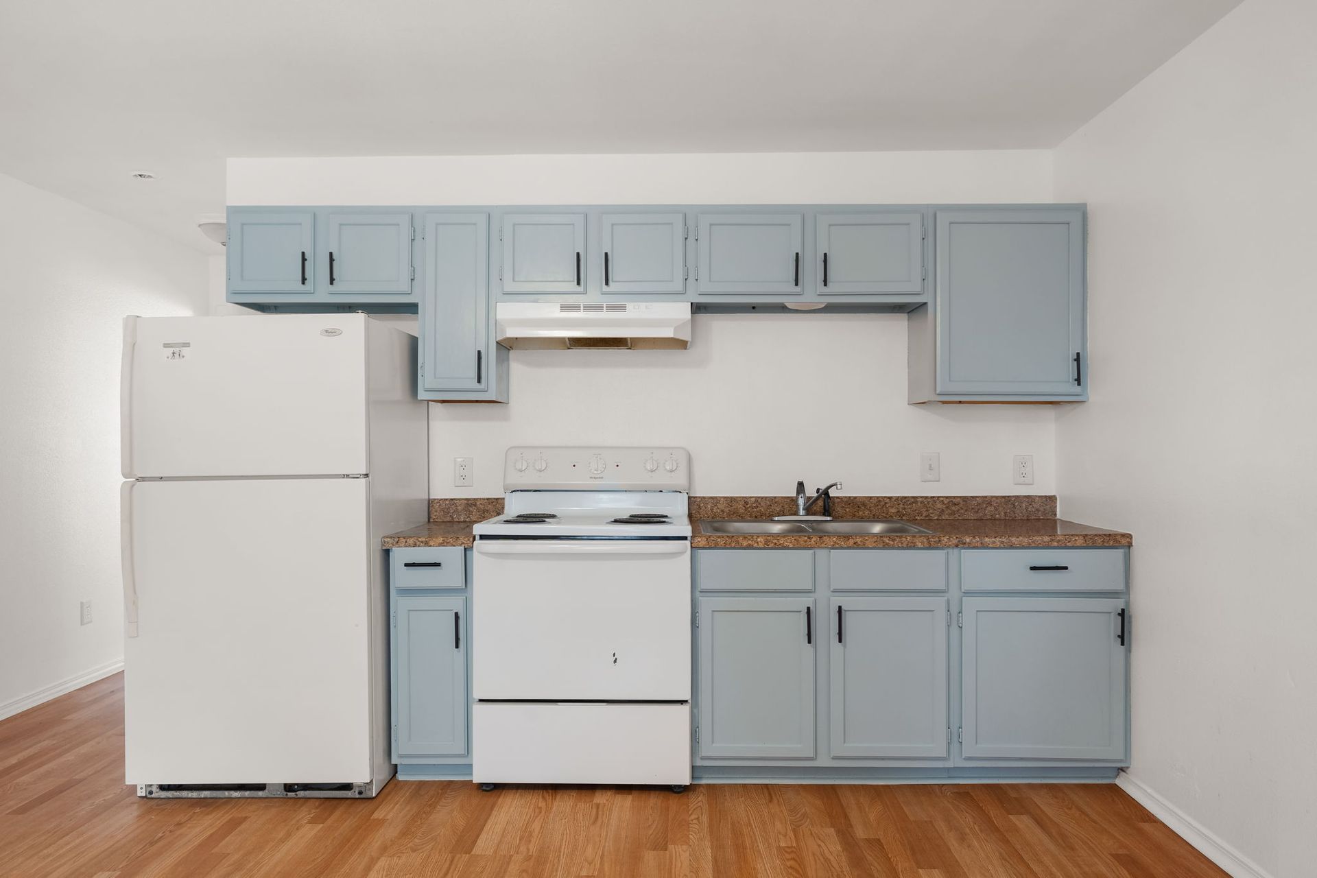 An empty kitchen with blue cabinets and a white refrigerator