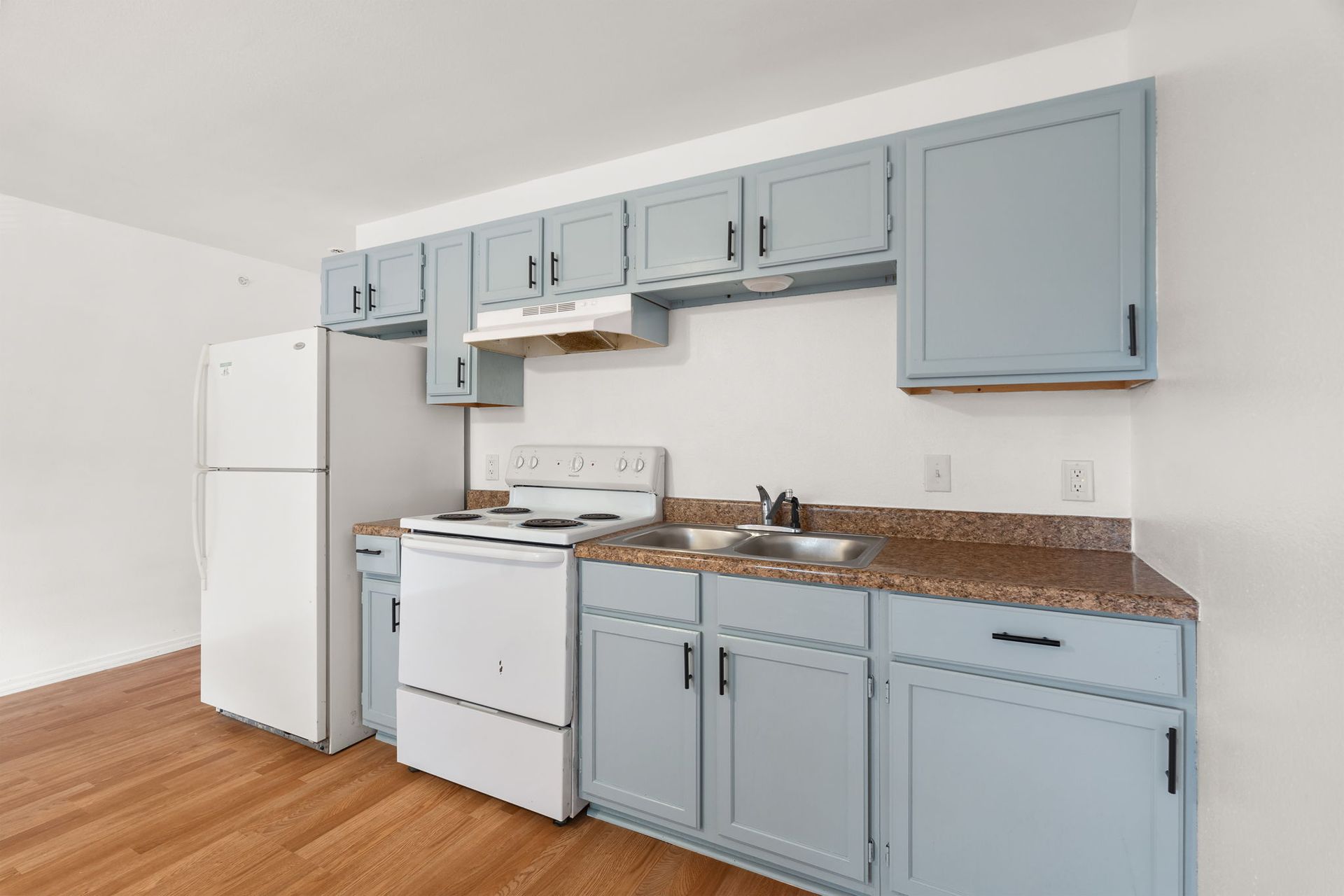 A kitchen with blue cabinets , white appliances , and a refrigerator.