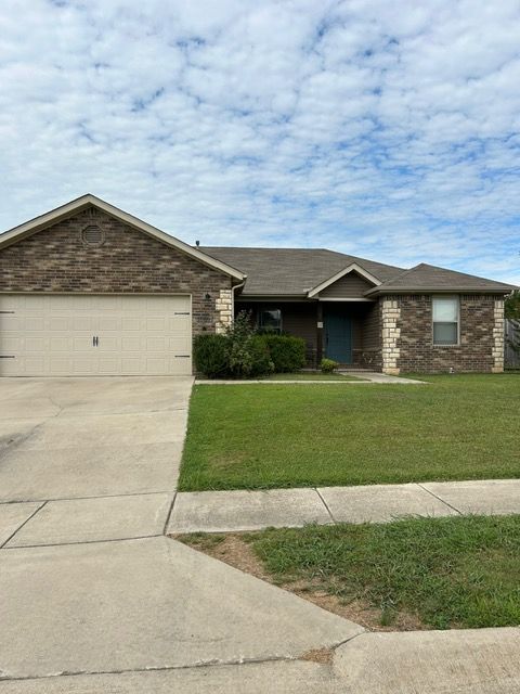 Single-story brick home with a two-car garage, green lawn, and cloudy sky.