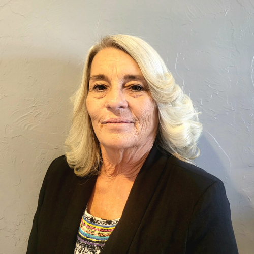 A woman with white hair is wearing a black jacket and a striped shirt.