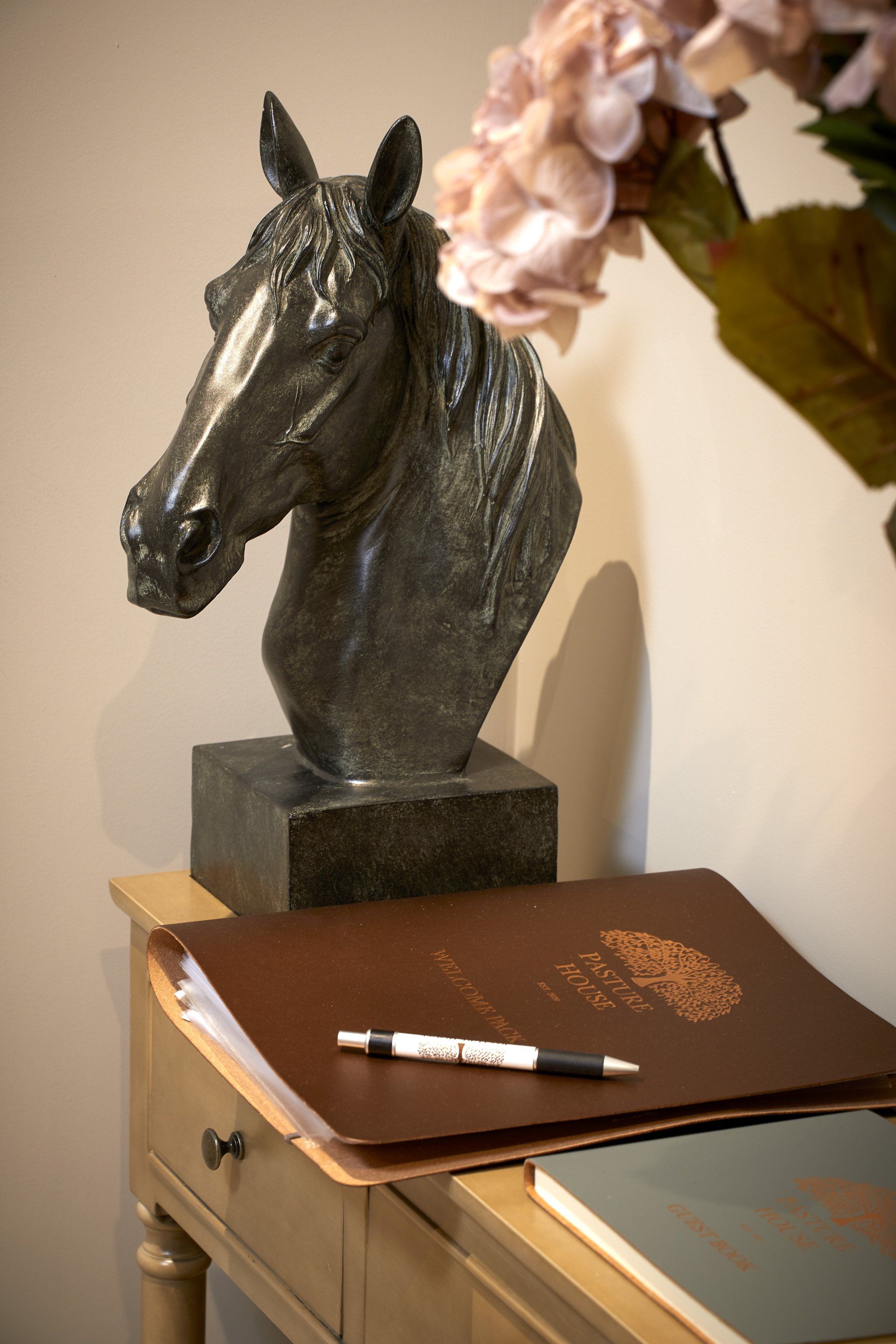 A statue of a horse 's head is on a table next to a pen and a book.