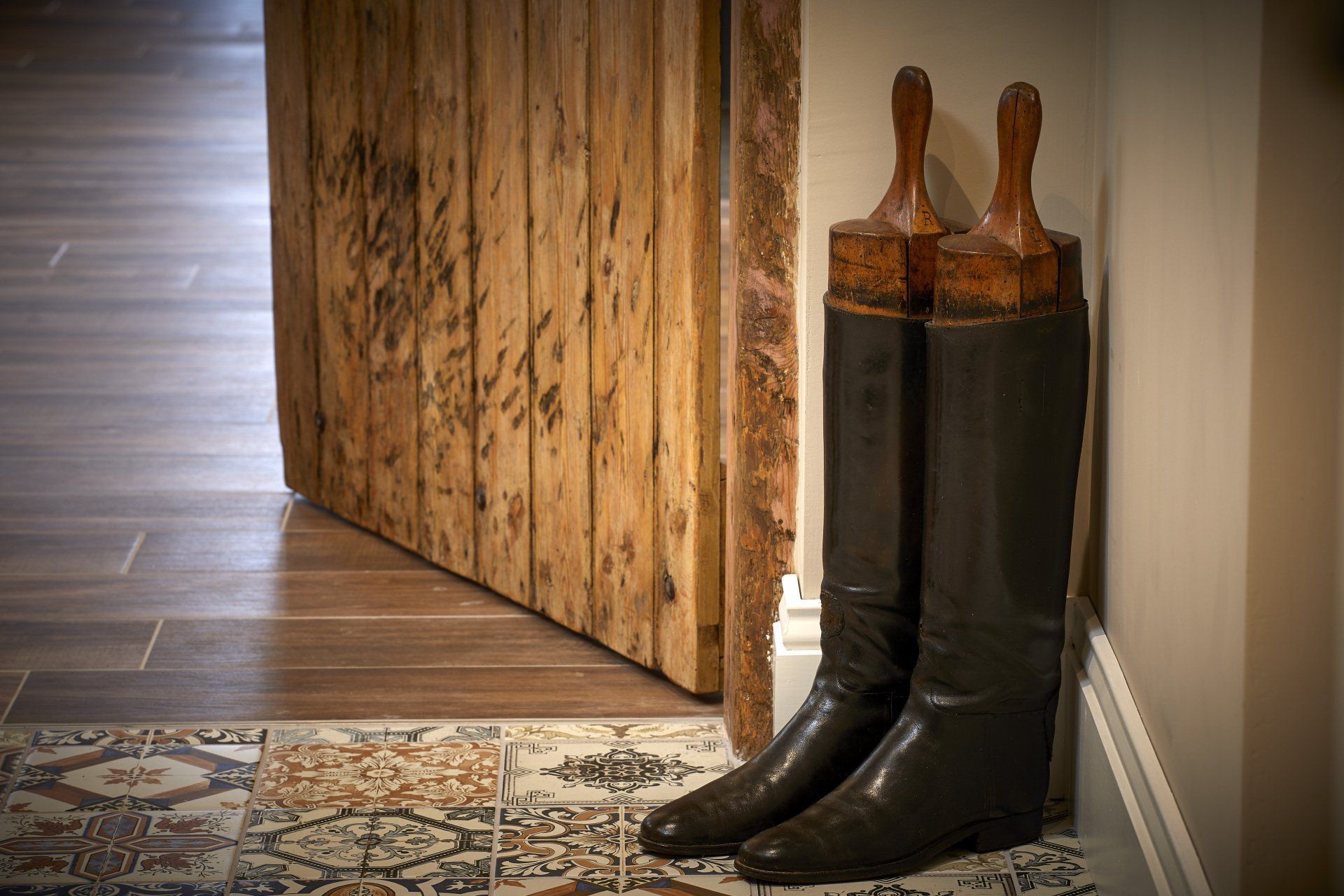 A pair of boots sitting on a tiled floor next to a wooden door.