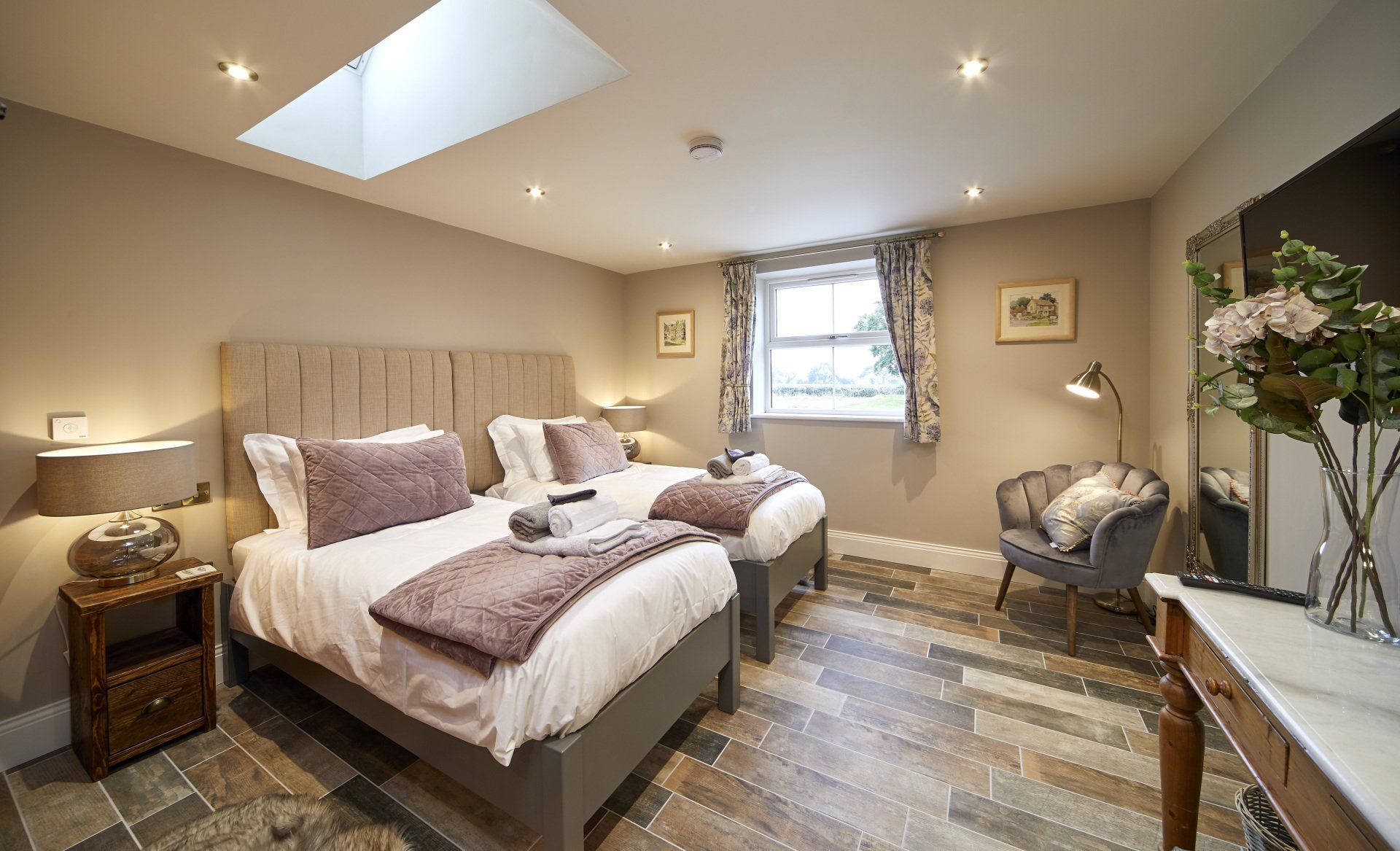 A bedroom with two beds , a chair , a table and a skylight.