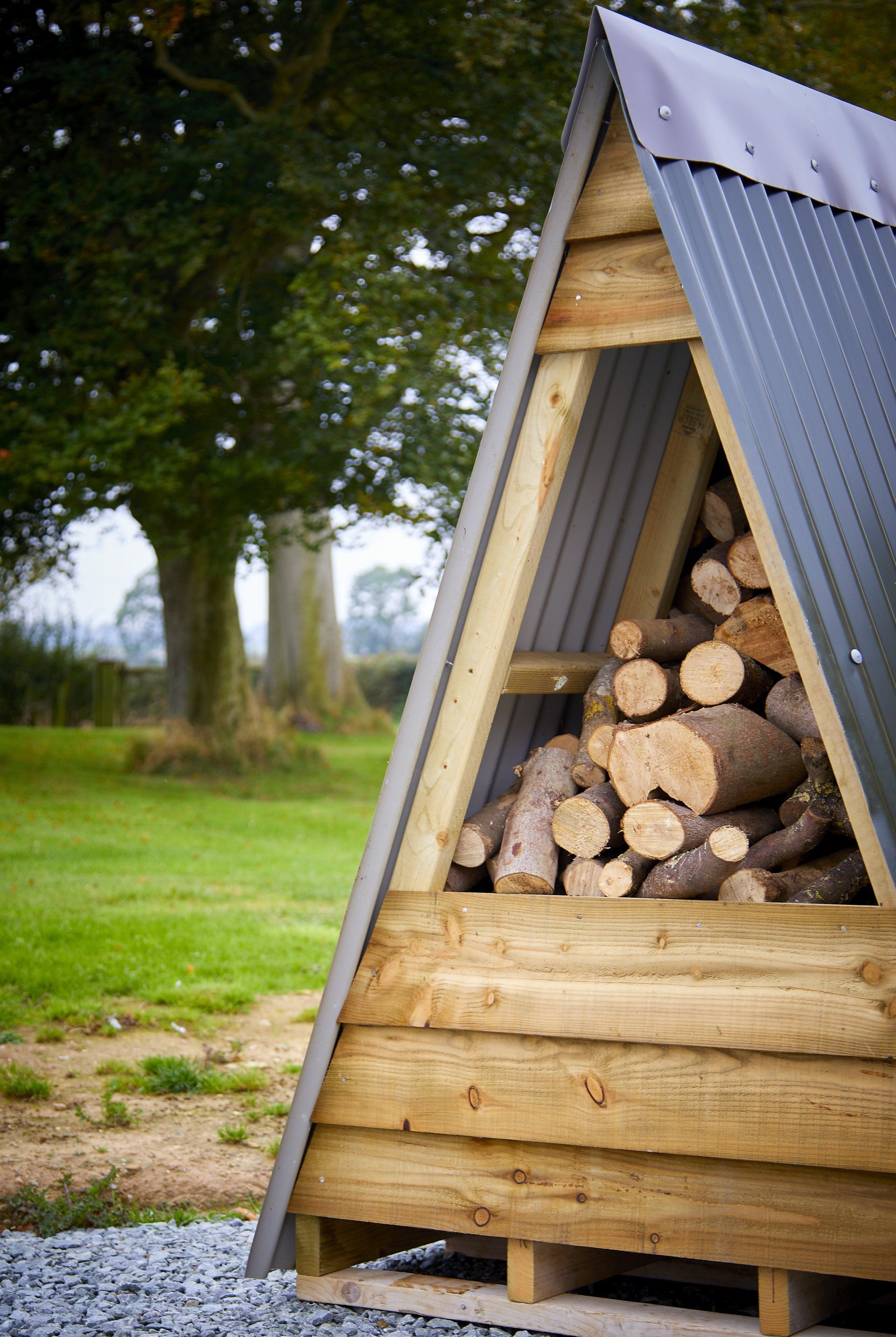 A triangle shaped wooden structure filled with logs in a field.