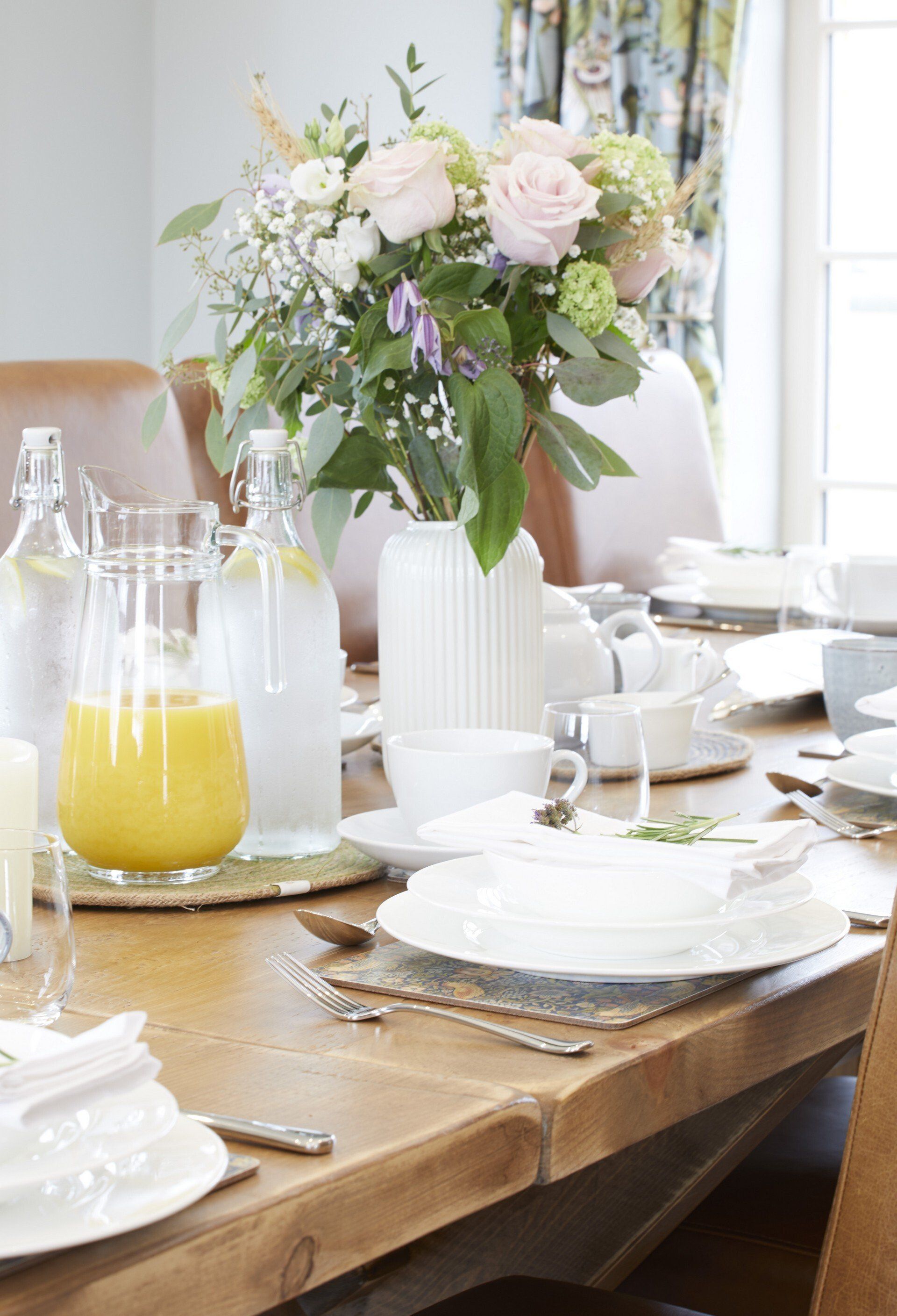 A dining room table with plates , utensils , a pitcher of orange juice and a vase of flowers.