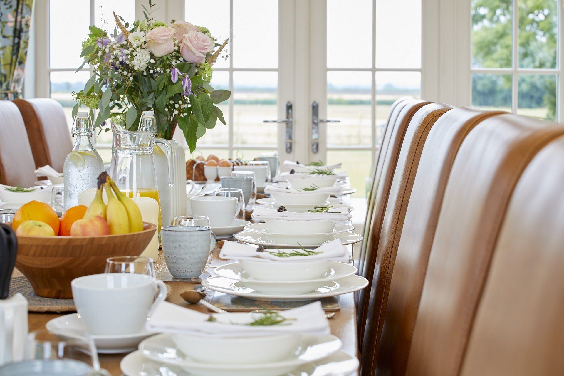 A long table with plates , bowls , and fruit on it.