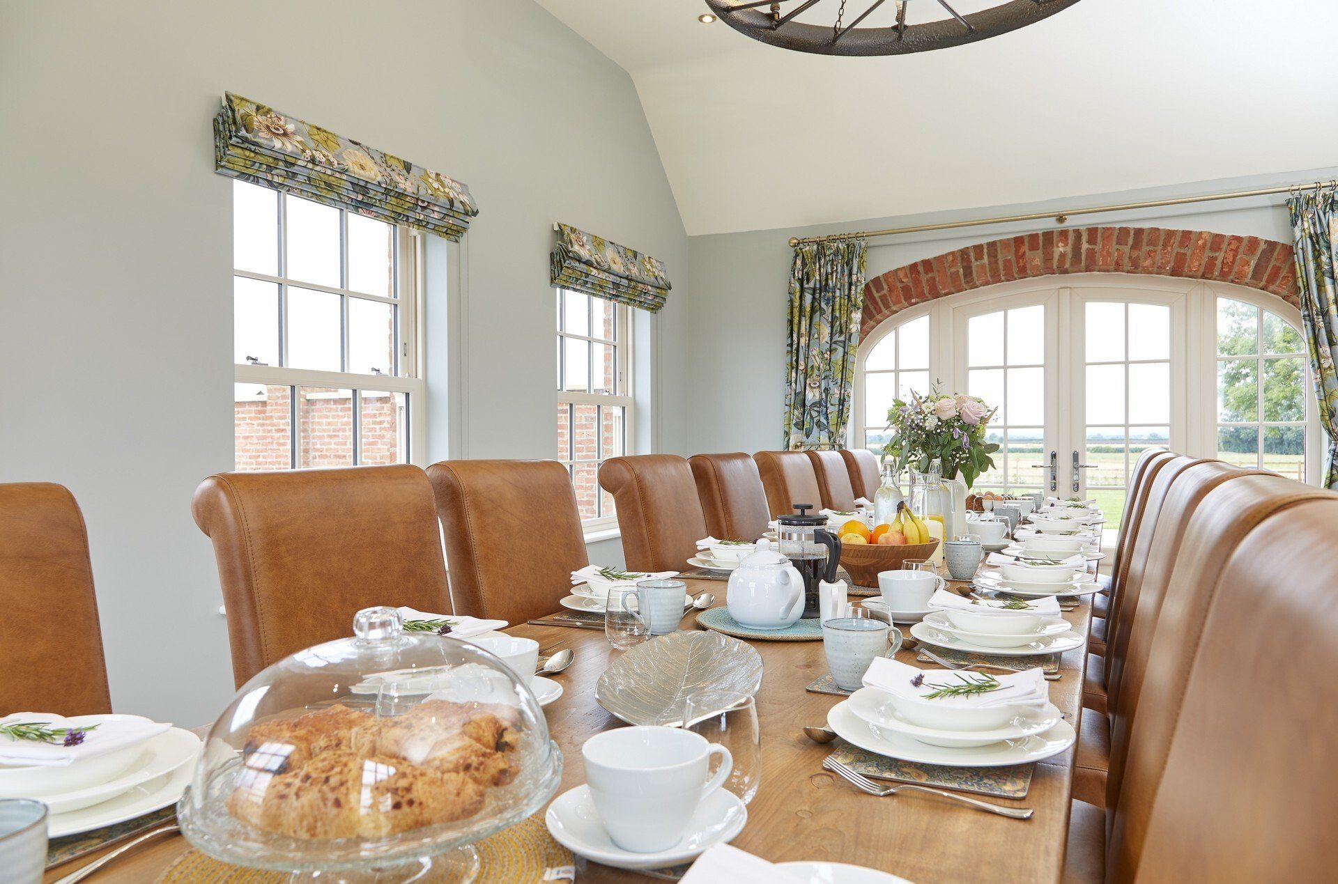 A long dining room table with plates , cups , and a cake on it.