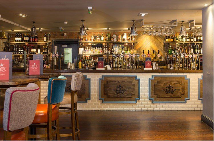 A bar with a lot of bottles on the shelves and tables and chairs.