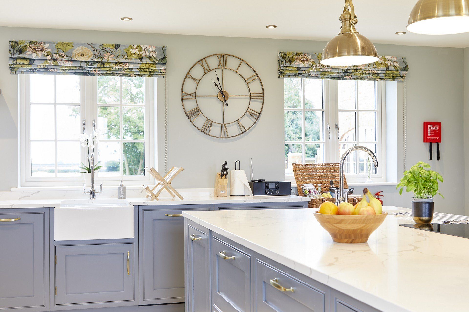 A kitchen with a clock on the wall and a bowl of fruit on the counter.