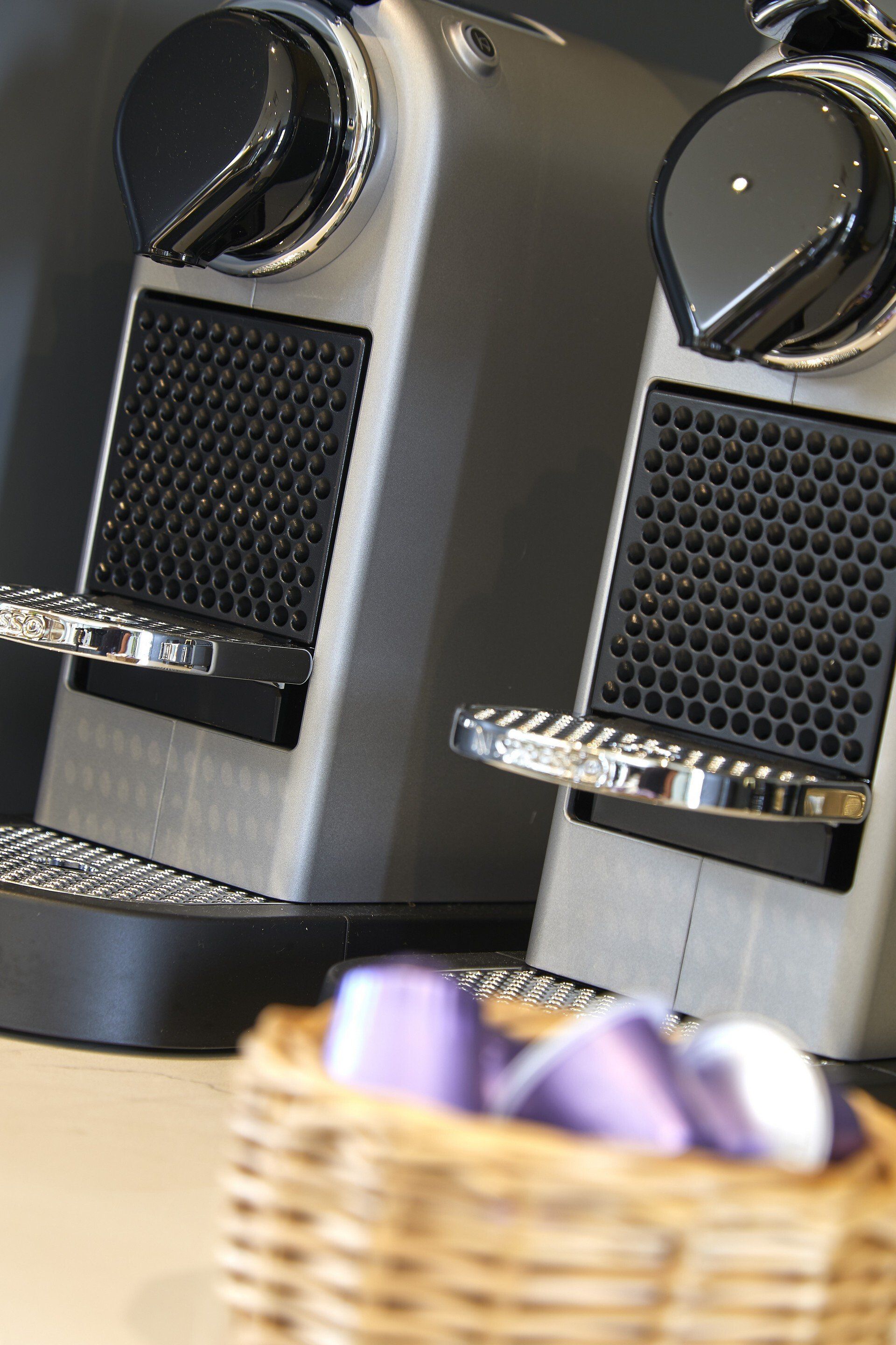 Two nespresso machines are next to a basket of purple capsules