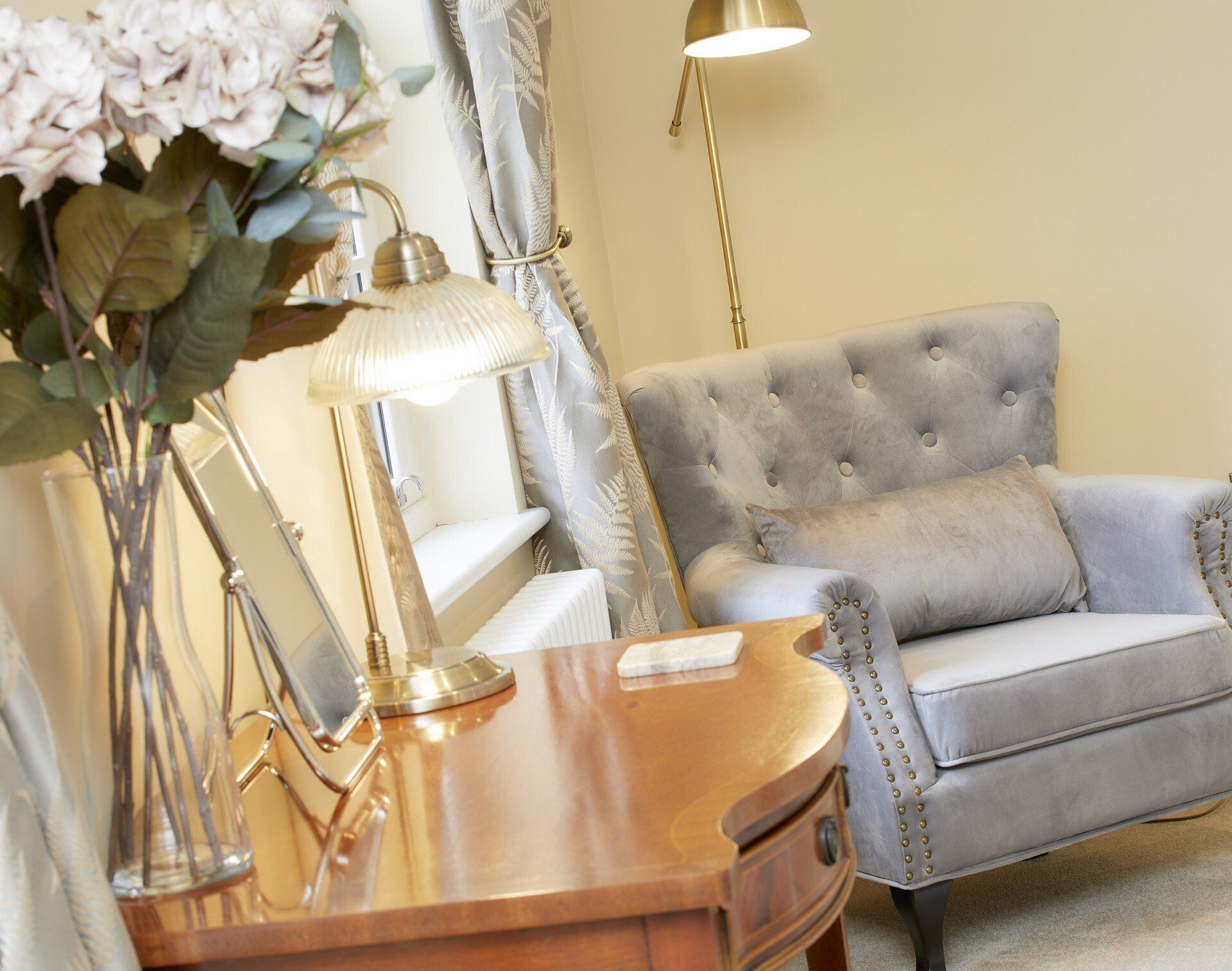 A living room with a chair and a table with a vase of flowers on it