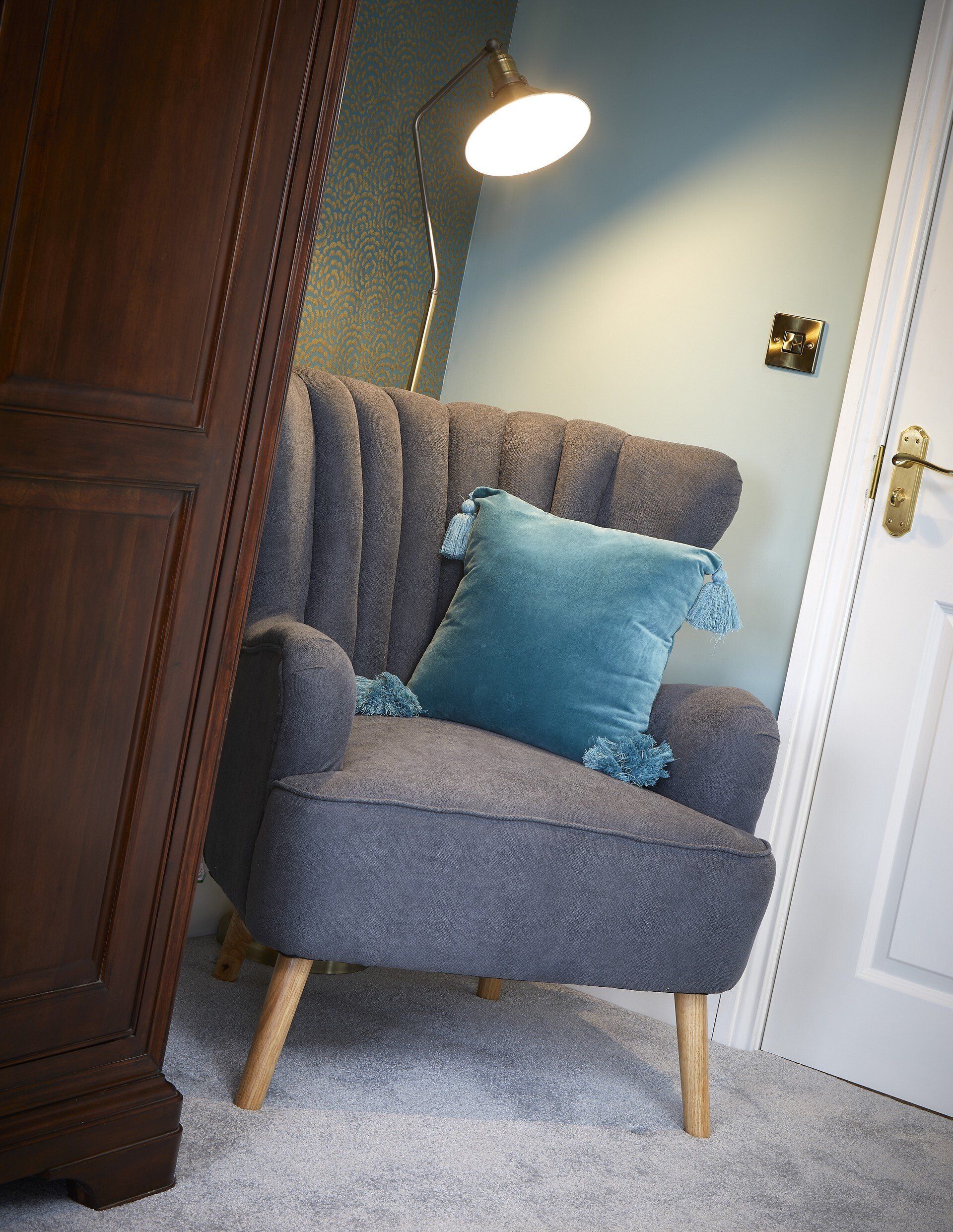 A chair with a blue pillow on it is in a room next to a lamp.