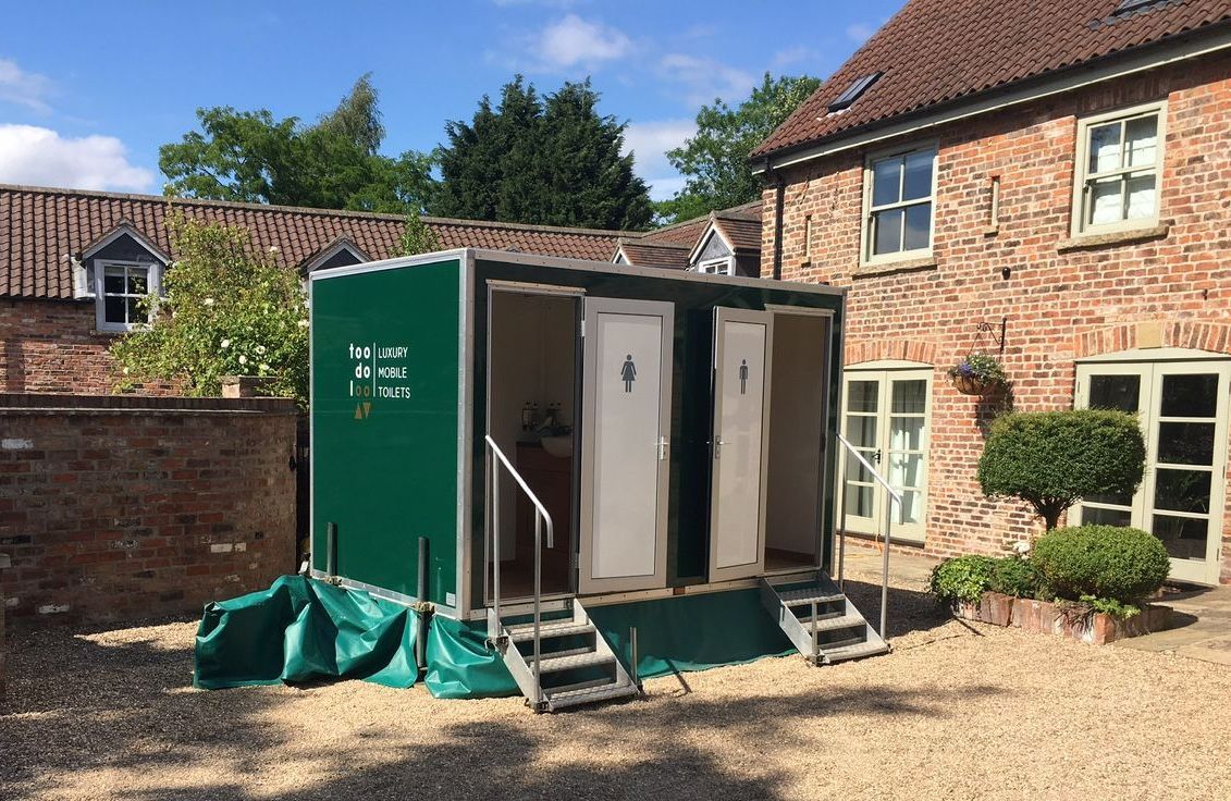 A portable toilet is parked in front of a brick house.