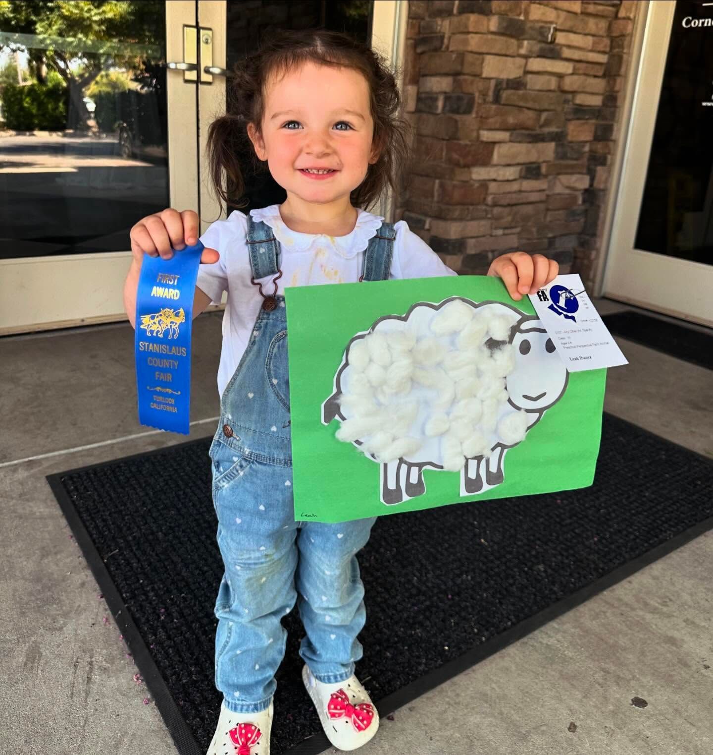 A little girl is holding a ribbon and a picture of a sheep