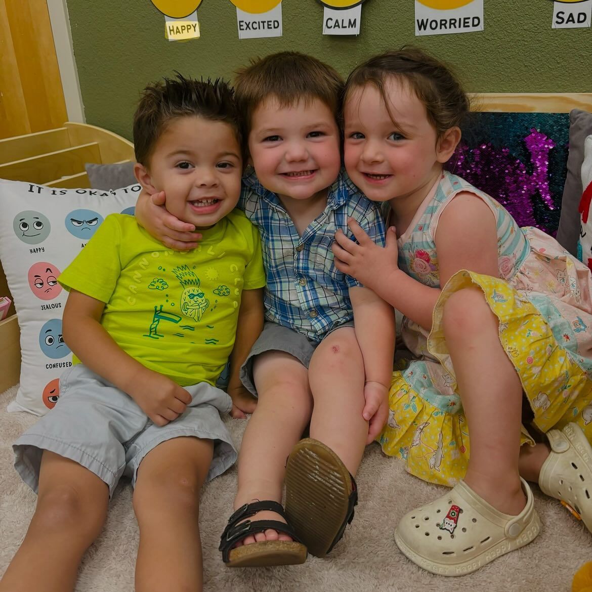 Three children are posing for a picture and one of them is wearing a yellow shirt with a frog on it
